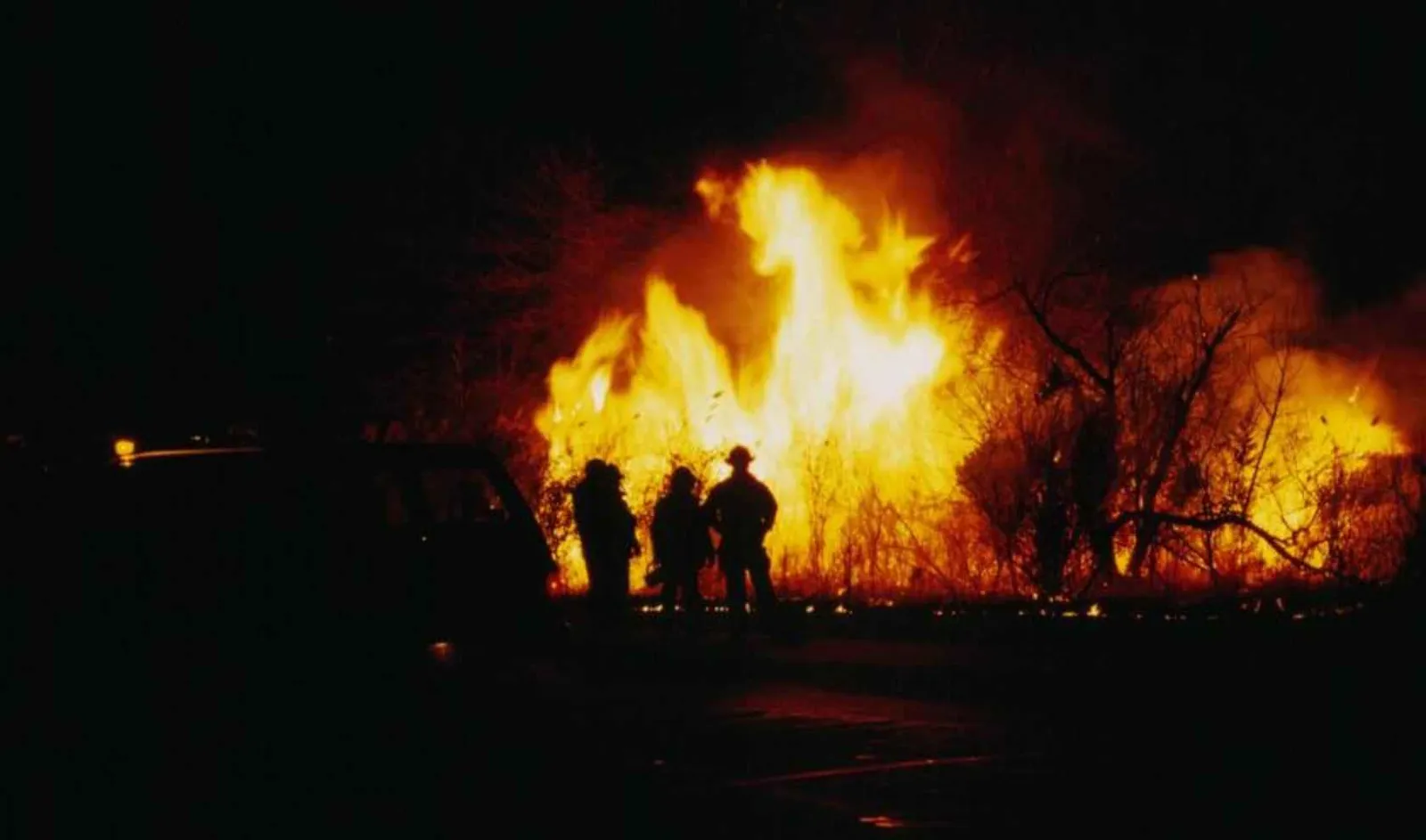 Vigili del fuoco in controluce davanti alle fiamme di un incendio notturno
